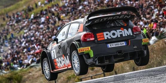 Citroën rally car airborne during a race, spectators in the background.